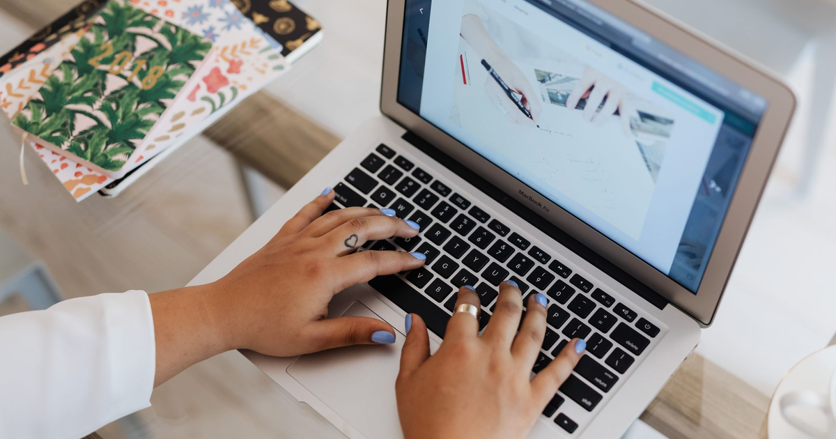 Close-up of hands typing on a laptop at a stylish office desk with notebooks.