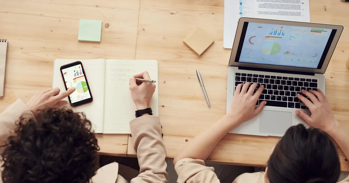 Overhead shot of two colleagues collaborating with devices and notes in a business meeting.