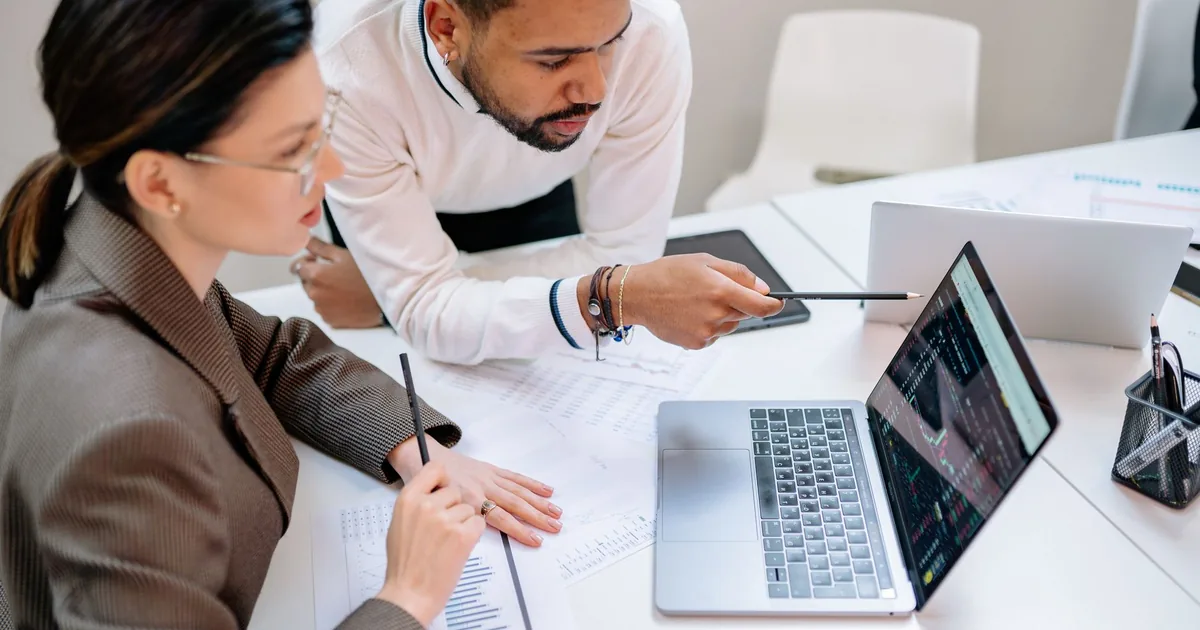 Business professionals discussing data at a desk with a laptop.
