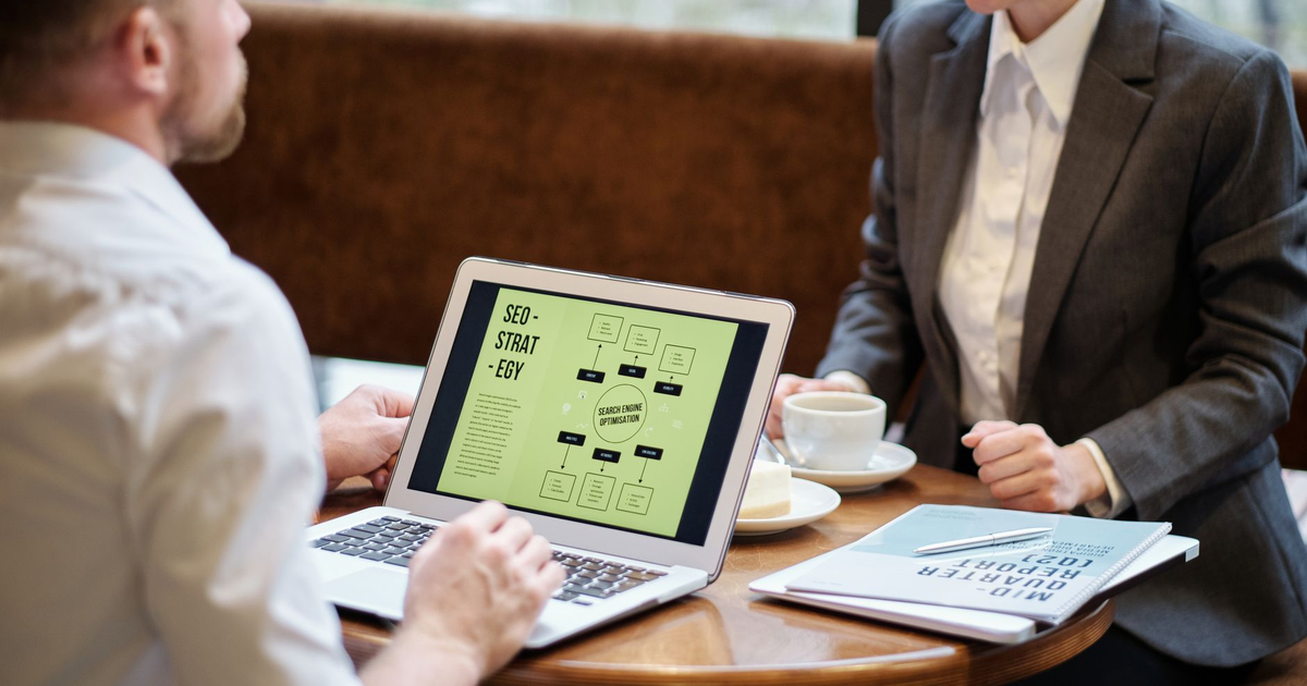 A man and woman engaged in a business meeting discussing SEO strategy in a cozy cafe setting.
