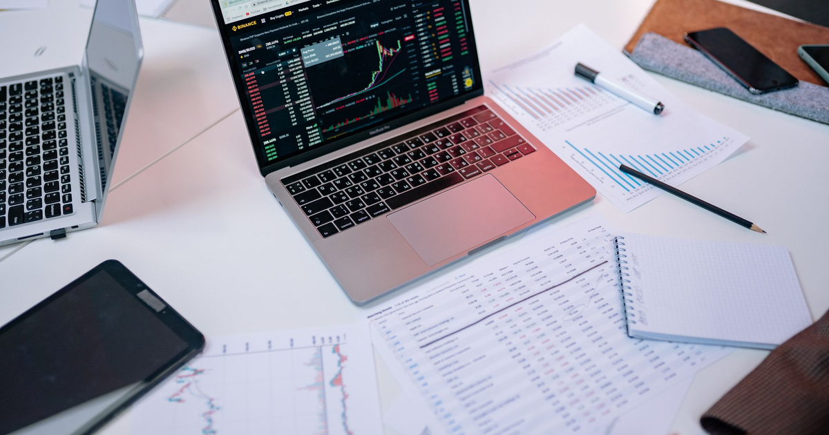 Laptops on a desk displaying stock market charts and financial documents.