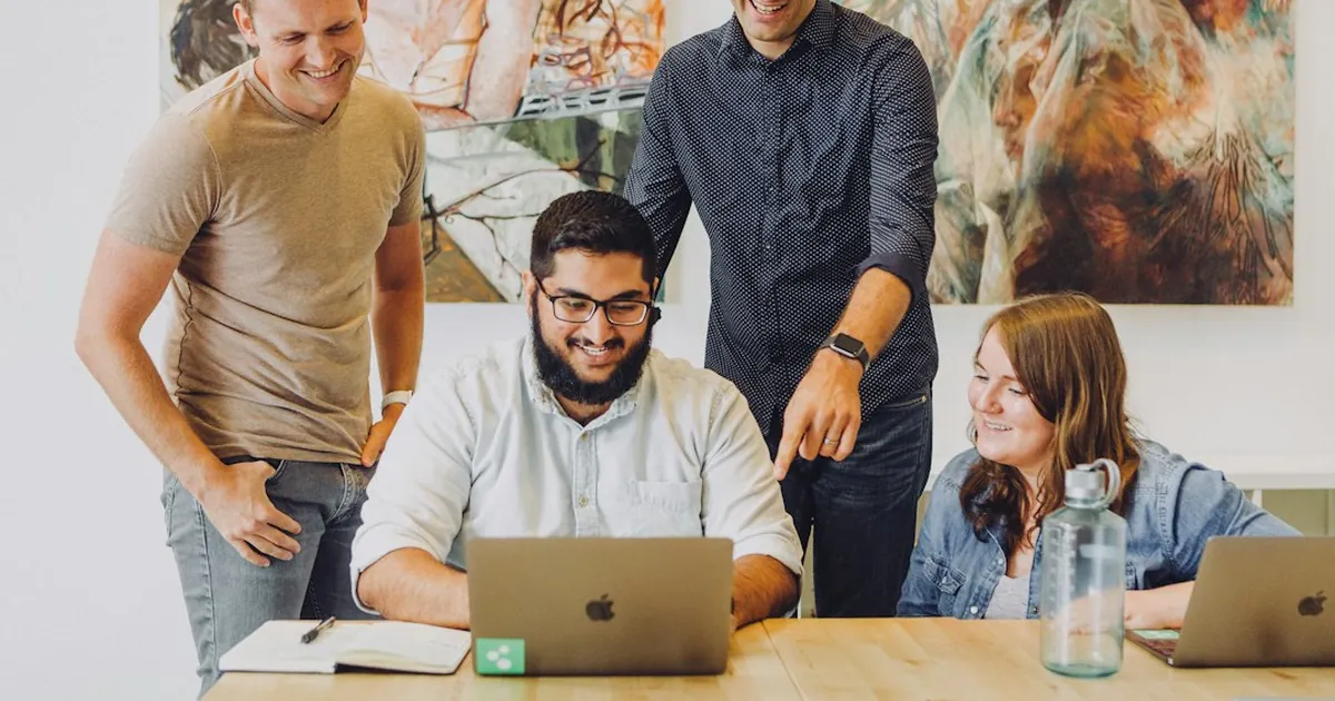 four coworkers smiling around laptop at table