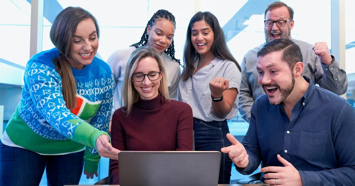 men and women sitting and standing while staring at laptop